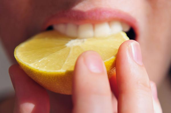 A young woman eats a slice of sour lemon with her teeth